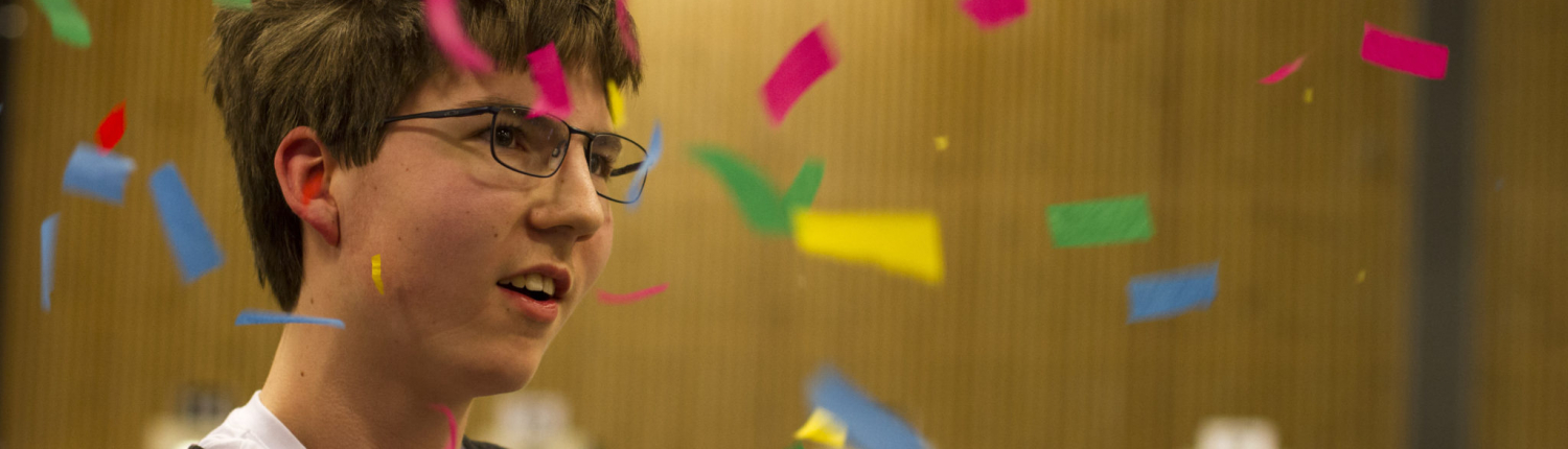 Bilde av en smilende Thomas Peelen mens han holder en kurv full av premier og konfettien regner rundt